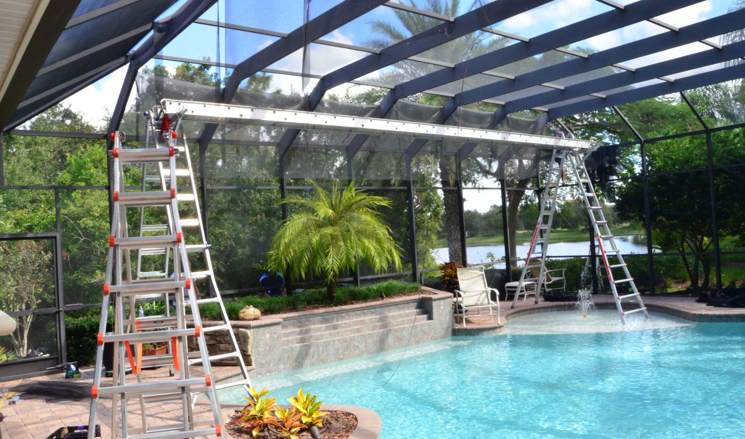 Pool cage screen repair with ladders set up over a swimming pool